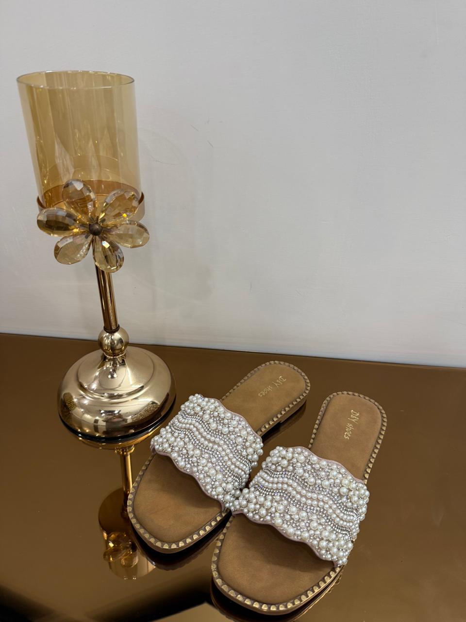 tep into effortless elegance with these beautifully crafted pearl embellished slide sandals. Designed with intricate hand-placed pearl detailing, these slides add a luxurious touch to your everyday and festive outfits. The soft cushioned sole ensures all-day comfort, while the open-toe design keeps your look light and stylish. Perfect for pairing with ethnic wear like kurtas and sarees or even modern outfits, these slides are your go-to choice for weddings, brunches, and casual outings. The subtle metallic base enhances the overall sophistication, making them a must-have addition to your footwear collection. Key Features: Premium pearl embellishment design Comfortable cushioned footbed Lightweight and easy slip-on style Durable sole for everyday wear Ideal for festive, ethnic & casual looks